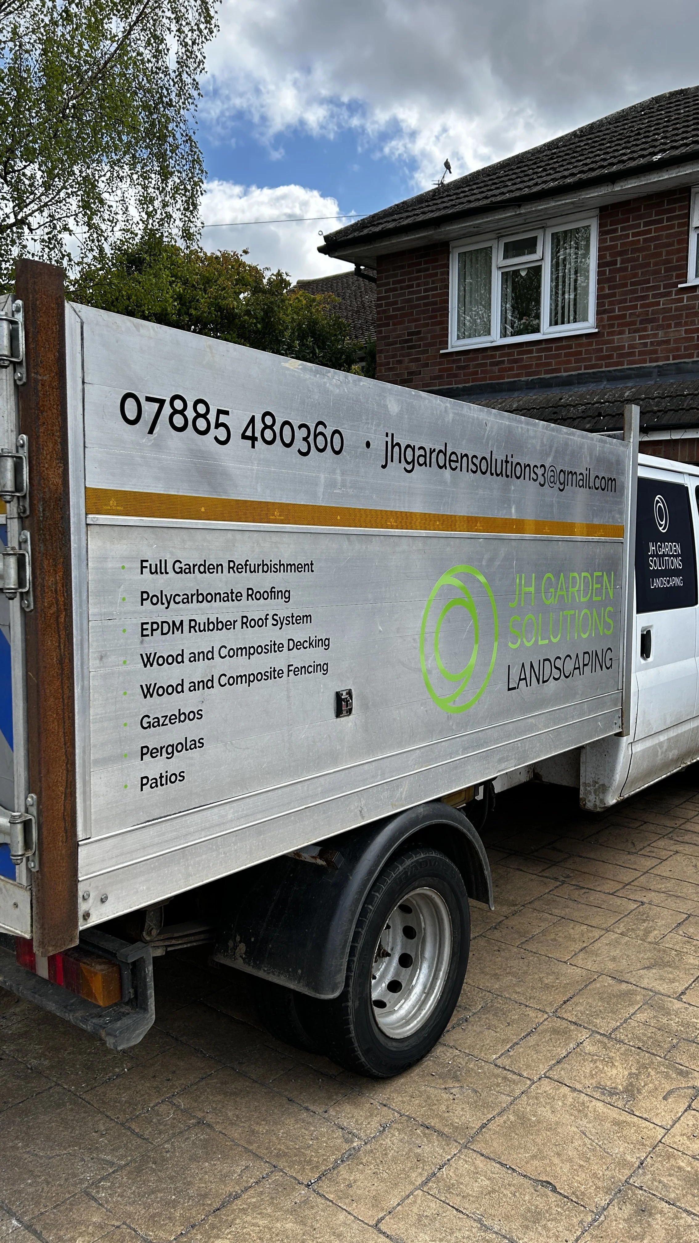 A landscaping company's truck parked on a driveway, displaying services like garden refurbishment, roofing, decking, fencing, gazebos, pergolas, and patios with contact information and email.