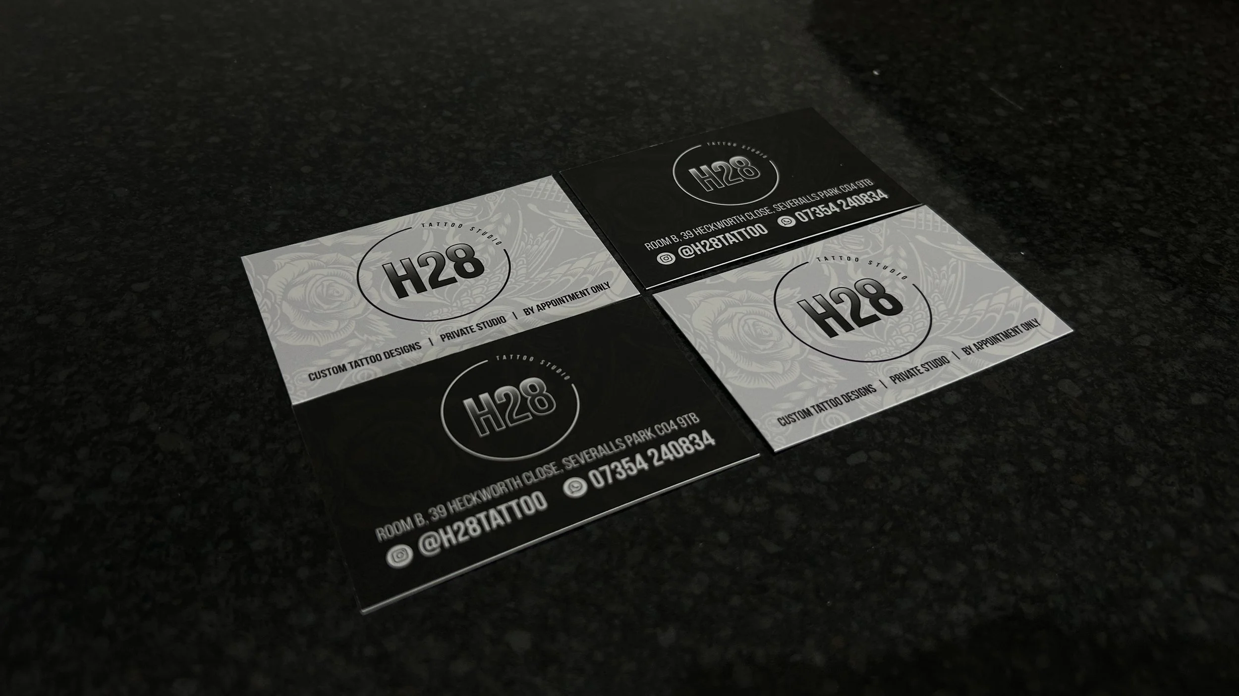 Close-up of three H28 tattoo studio appointment cards on a dark surface, featuring studio name, address, contact information, and social media handle.