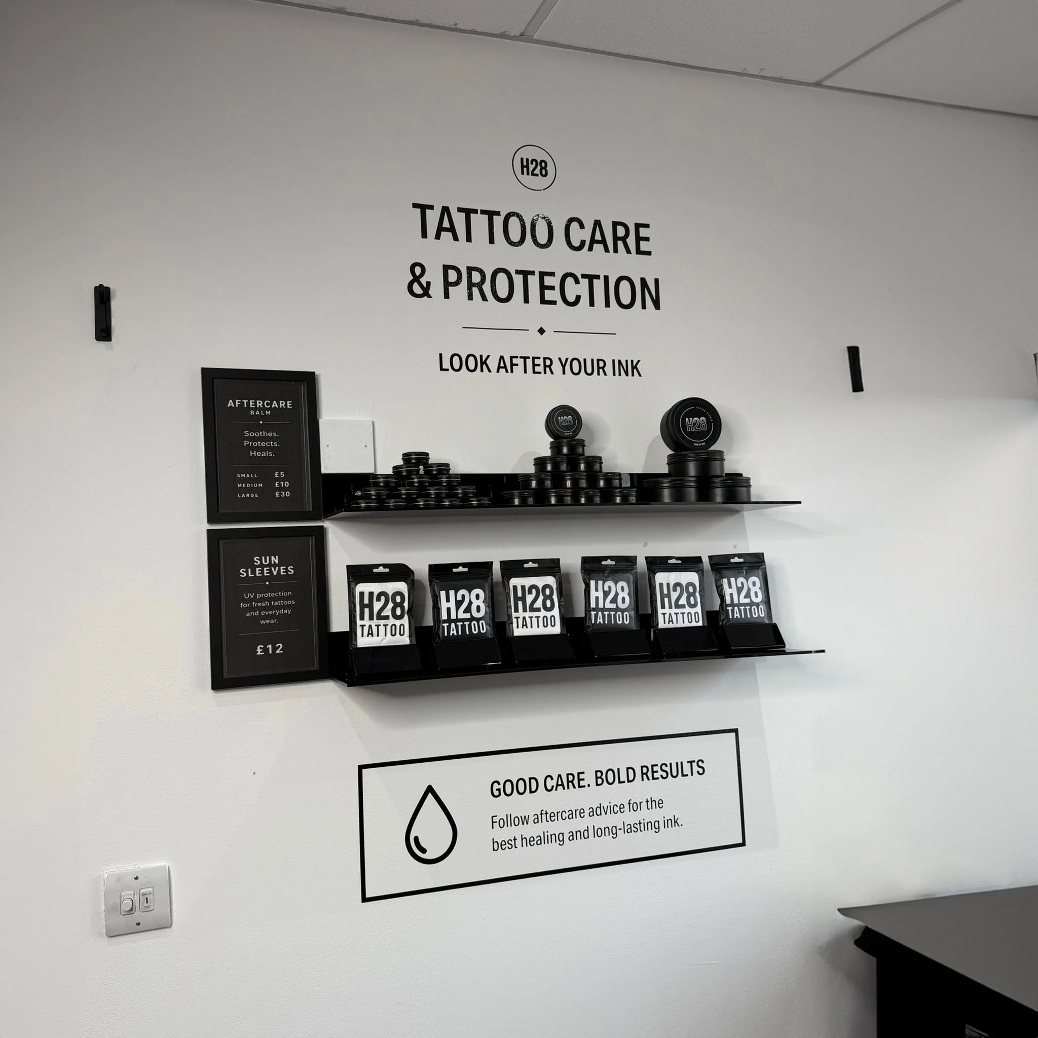 A wall inside a tattoo care shop with signs providing aftercare instructions and product information, including a shelf with tattoo aftercare balm containers.