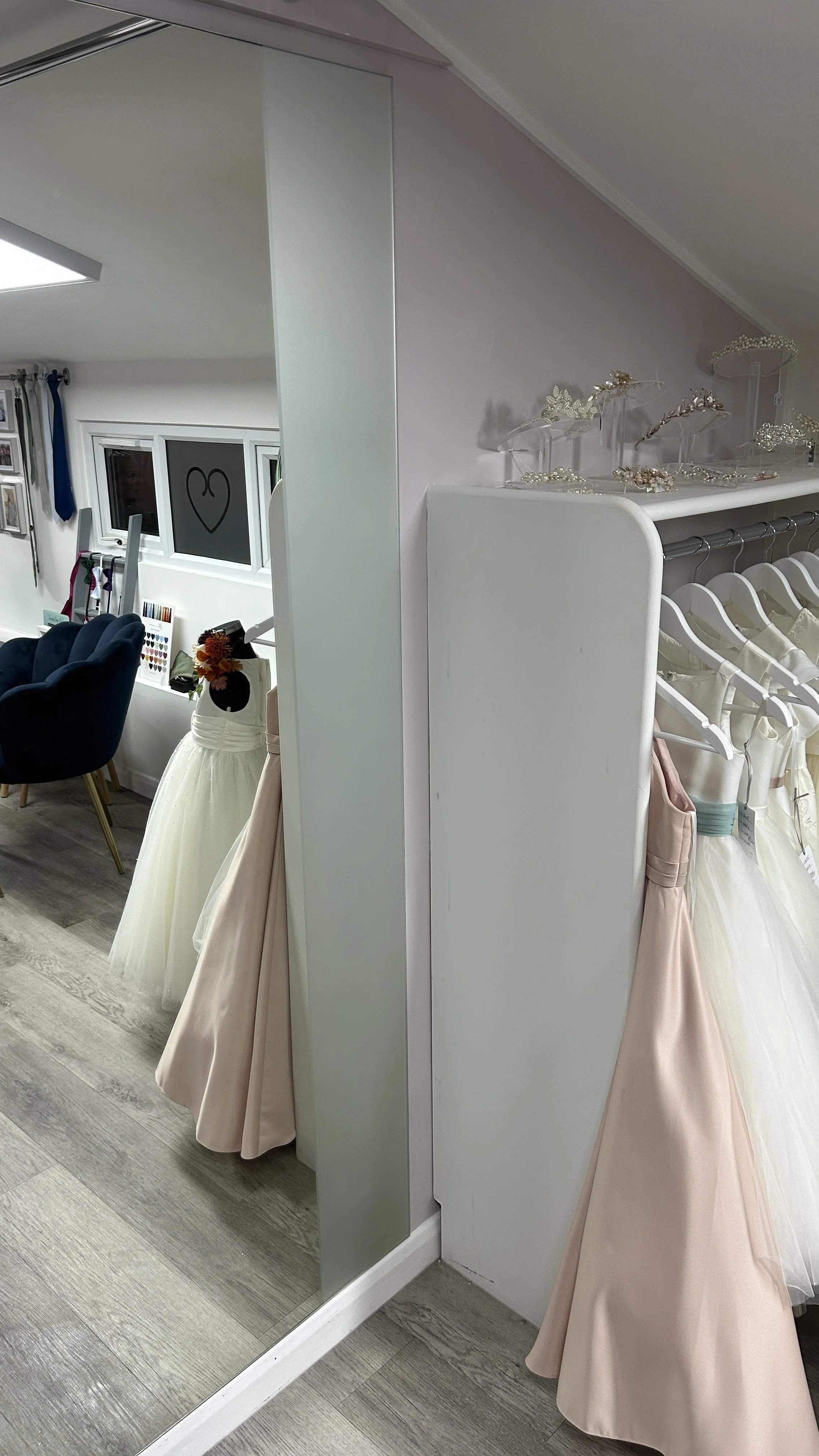 Display of elegant cream and blush bridesmaid dresses with bead and floral headbands on a white rack in a bridal shop.