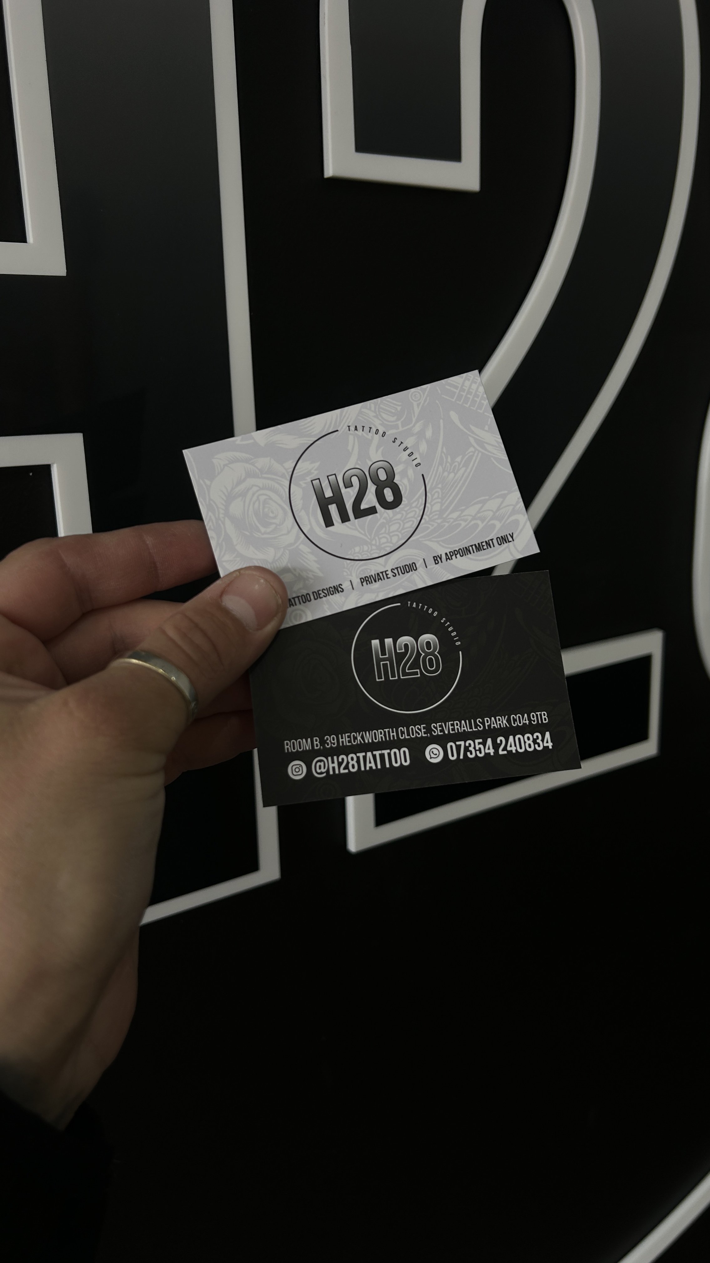Hand holding two business cards in front of a black and white striped background.