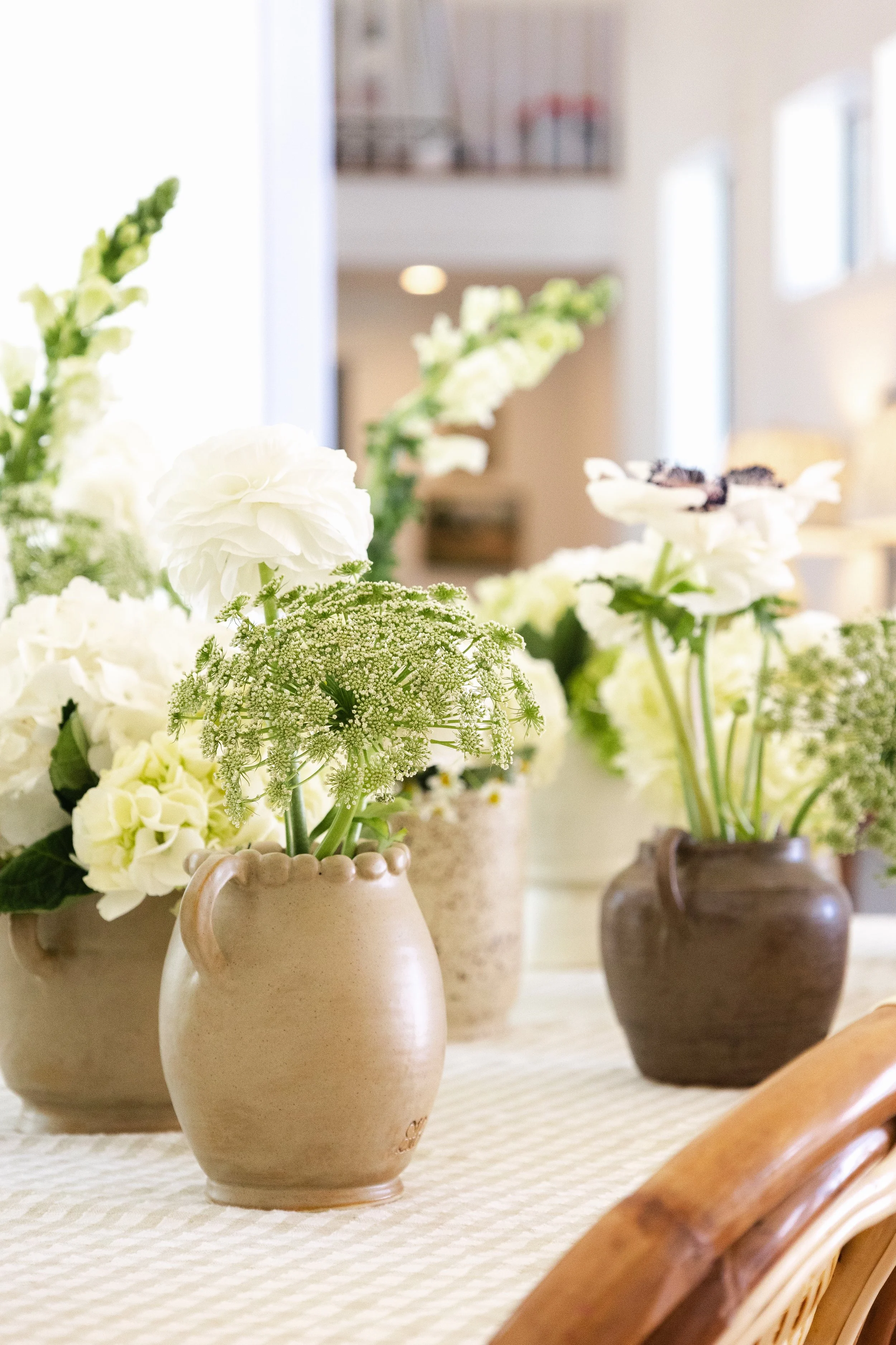 A table decorated with multiple vases of white flowers, set in a bright, airy room.