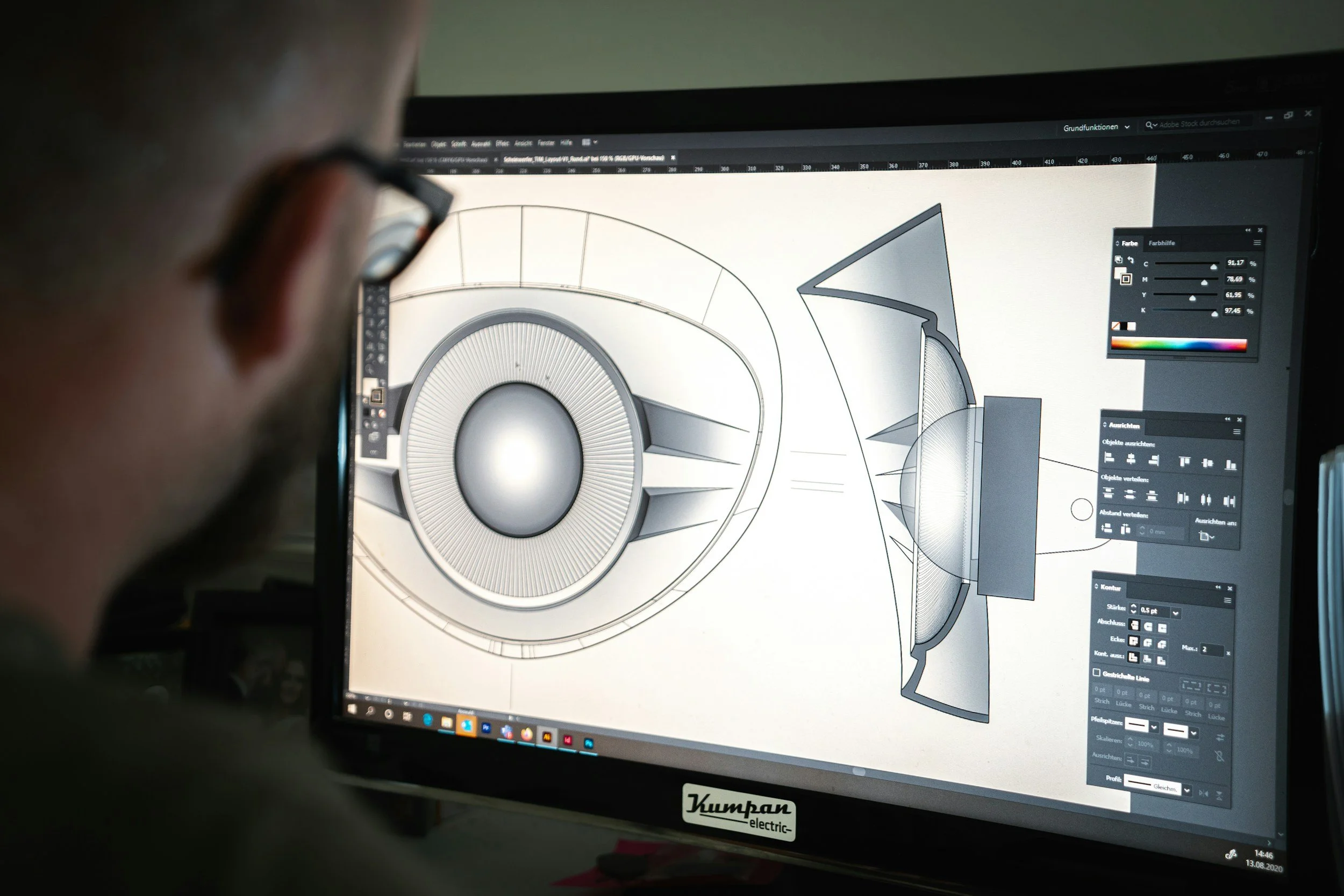 A person works on a computer screen displaying a technical design drawing of a circular object with detailed shading and diagram labels. The person is wearing glasses and has short hair. The workspace appears to be dimly lit.