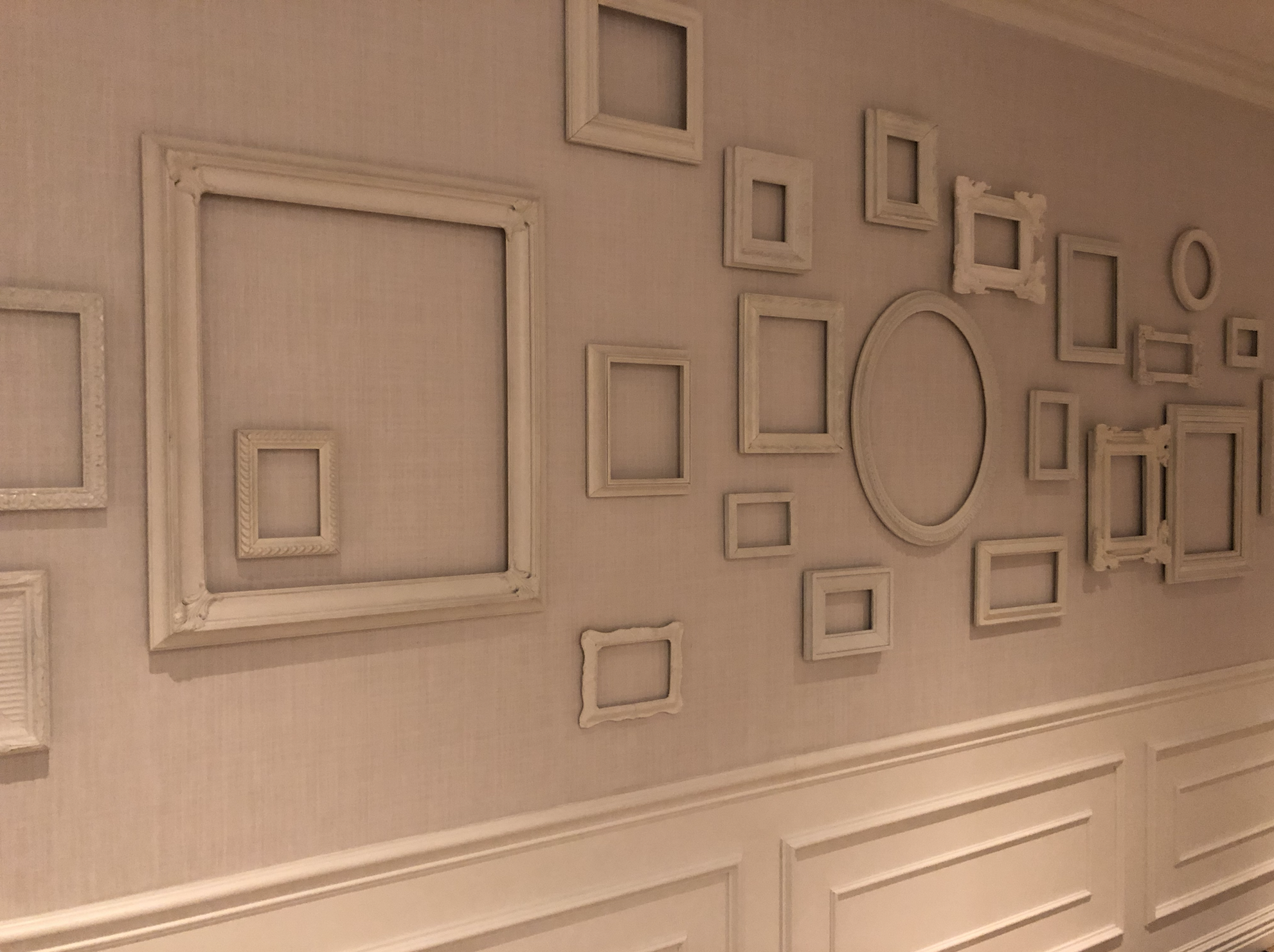 Hallway with empty gold picture frames hanging on white walls, suggesting space for something yet to be curated.