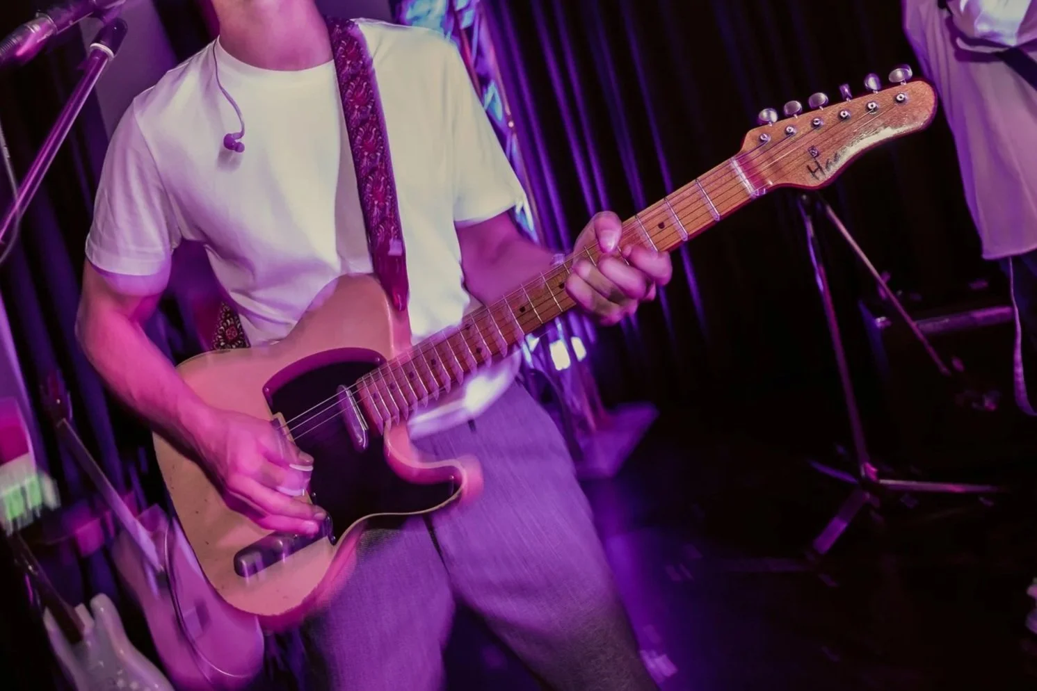 Musiker spielt E-Gitarre in einem dunklen Raum mit rotem und violettem Licht.