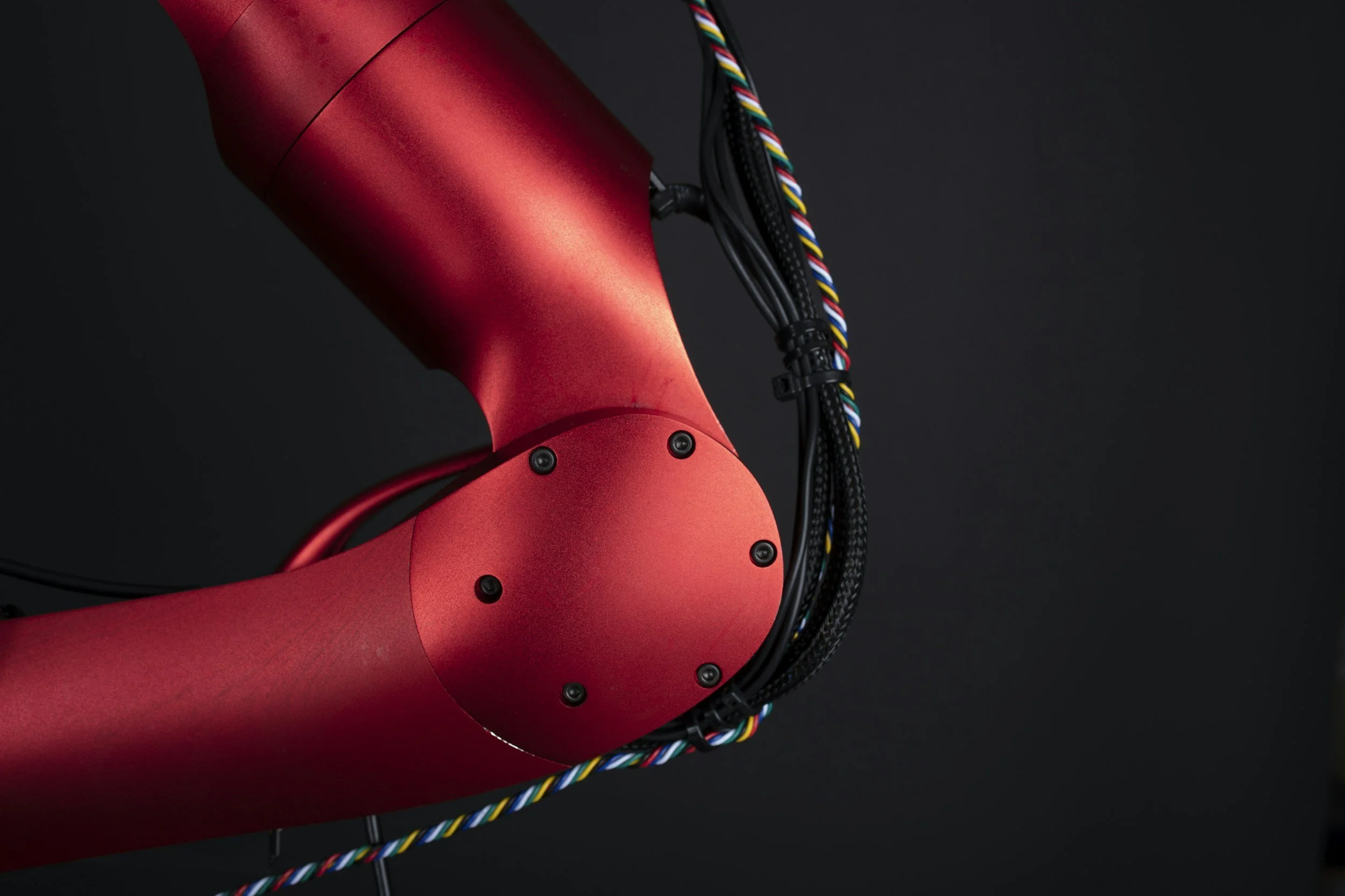 Close-up of a red robotic arm with black screws and multicolored wires on a dark background.