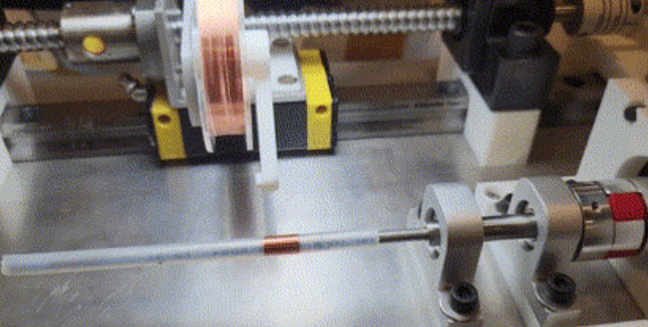 A machine with a long copper wire being wound onto a spool in a laboratory or manufacturing setting.