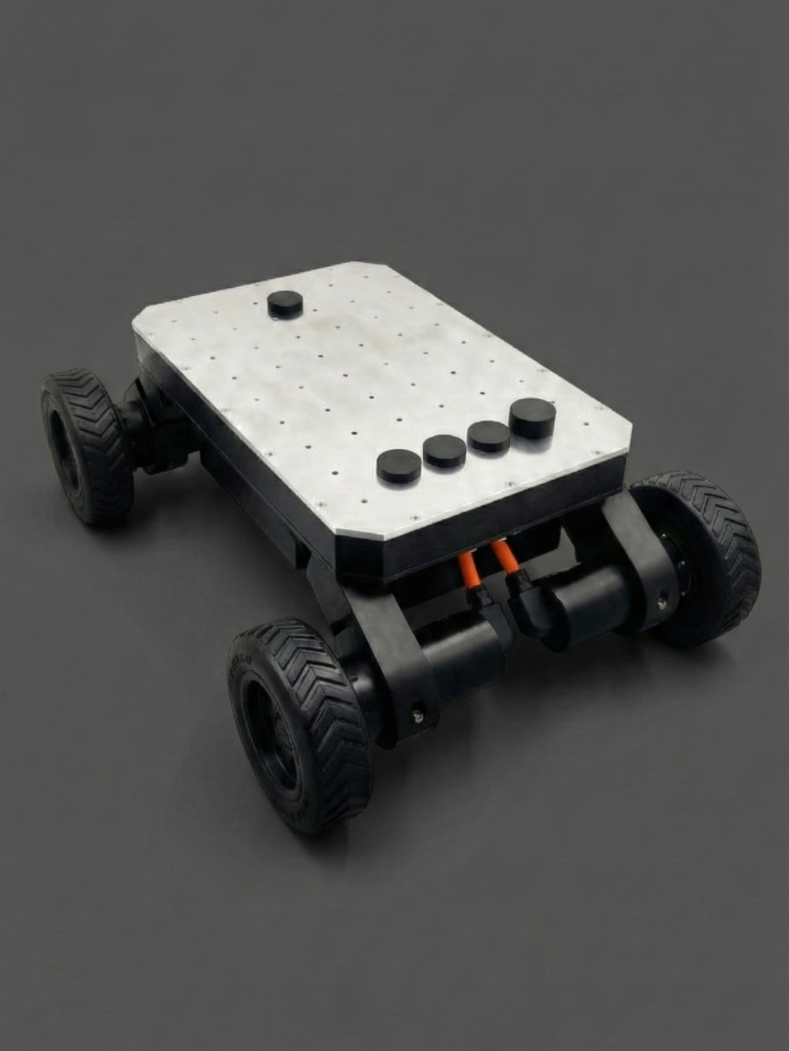 A small four-wheeled robot with a white top, black base, and orange wiring, on a dark surface.