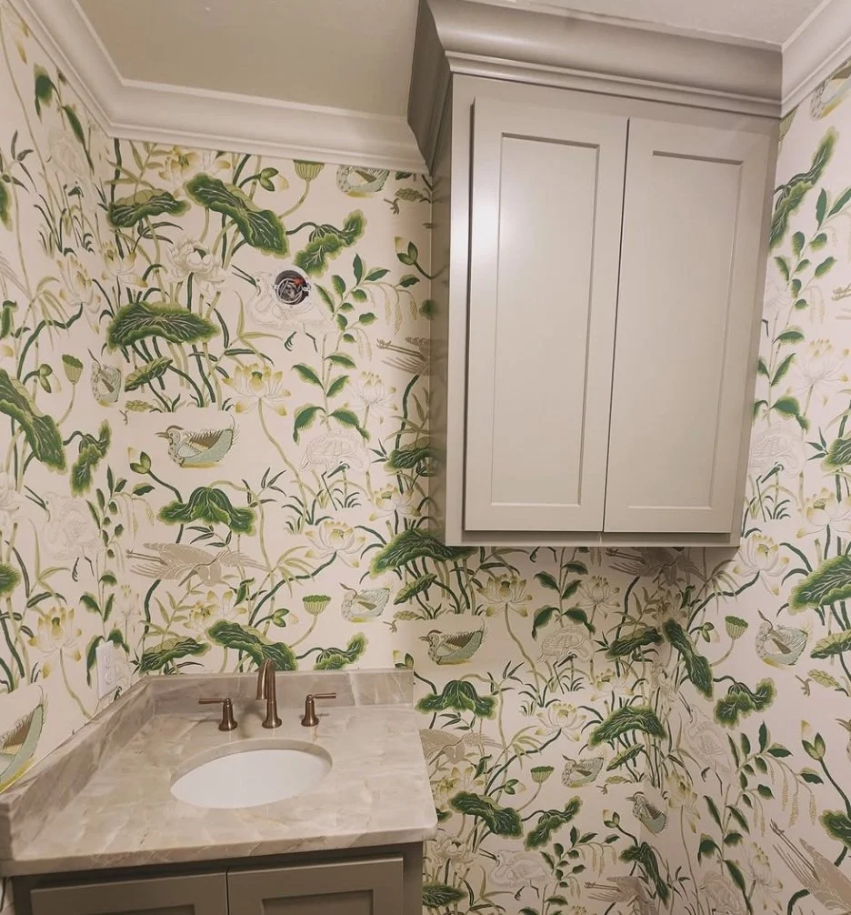 A small bathroom with floral wallpaper, gray cabinetry, a marble countertop with a sink, and a wall-mounted cabinet.