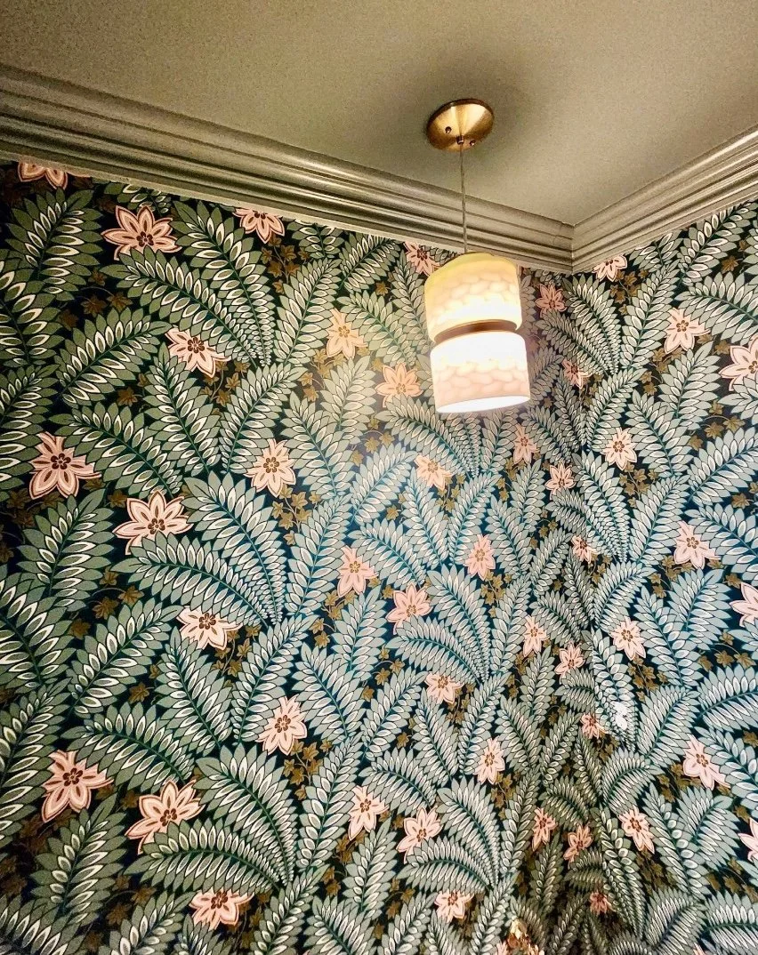 Floral wallpaper with green leaves and pink flowers, white crown molding, and a hanging light fixture with two cylindrical shades.