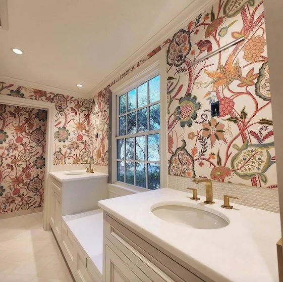 Bathroom with floral wallpaper, white vanity with a round sink, and a large window with a view of trees outside.