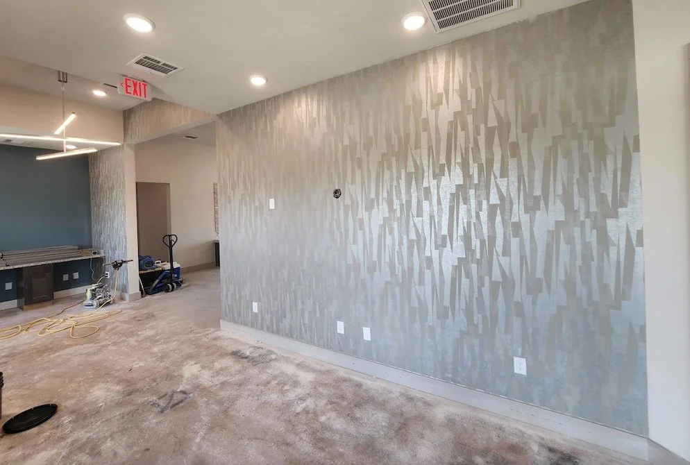 Empty room undergoing renovation with a textured gray wall, ceiling lights, and construction tools on the floor.