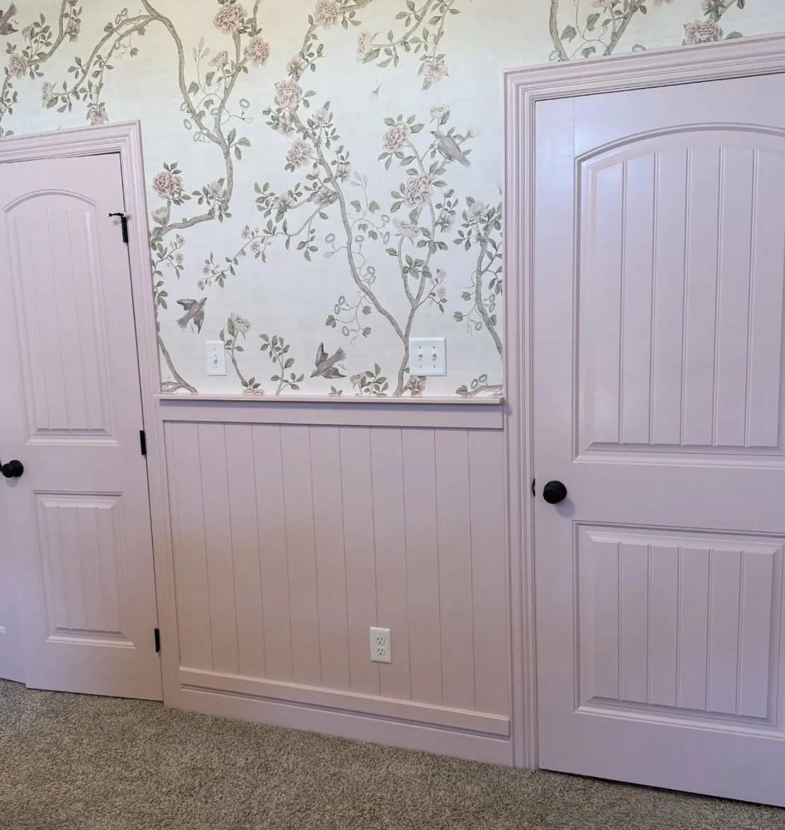 Interior wall with floral wallpaper, two doors with black knobs, and electrical outlets.