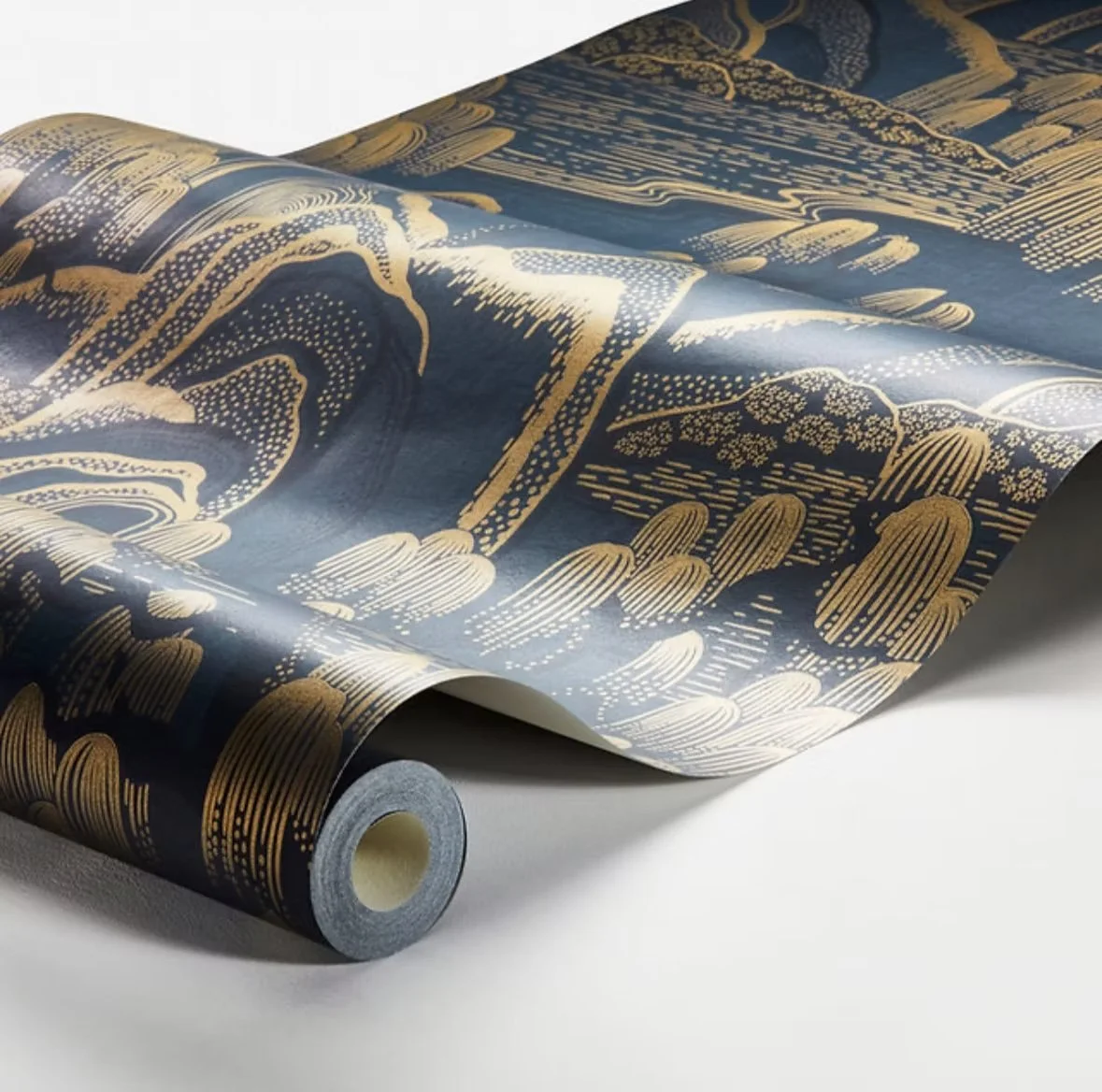 A roll of dark blue wallpaper with a gold, abstract landscape pattern, partially unrolled on a white surface.