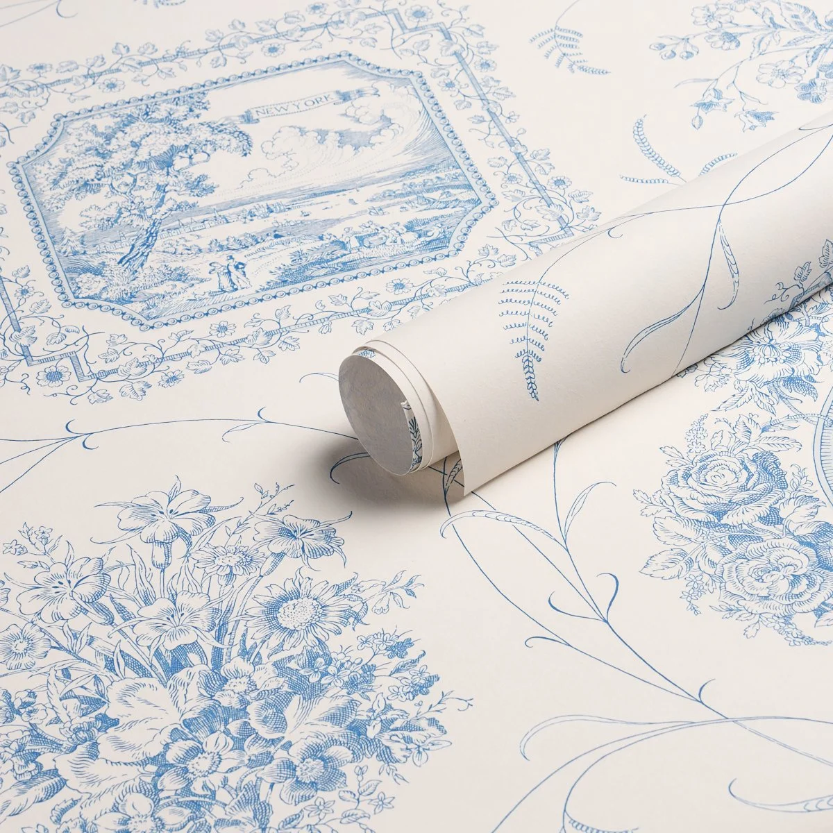 Schumacher Century Scenic Toile wallpaper in Blue, unfurled on a roll to show the New York vignette, floral frame, and paper texture, SKU 5018411