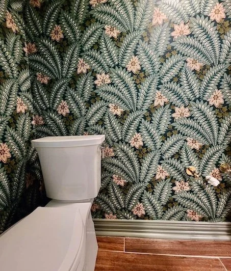 Close-up of a bathroom wall with tropical leaf and flower wallpaper next to a white toilet.