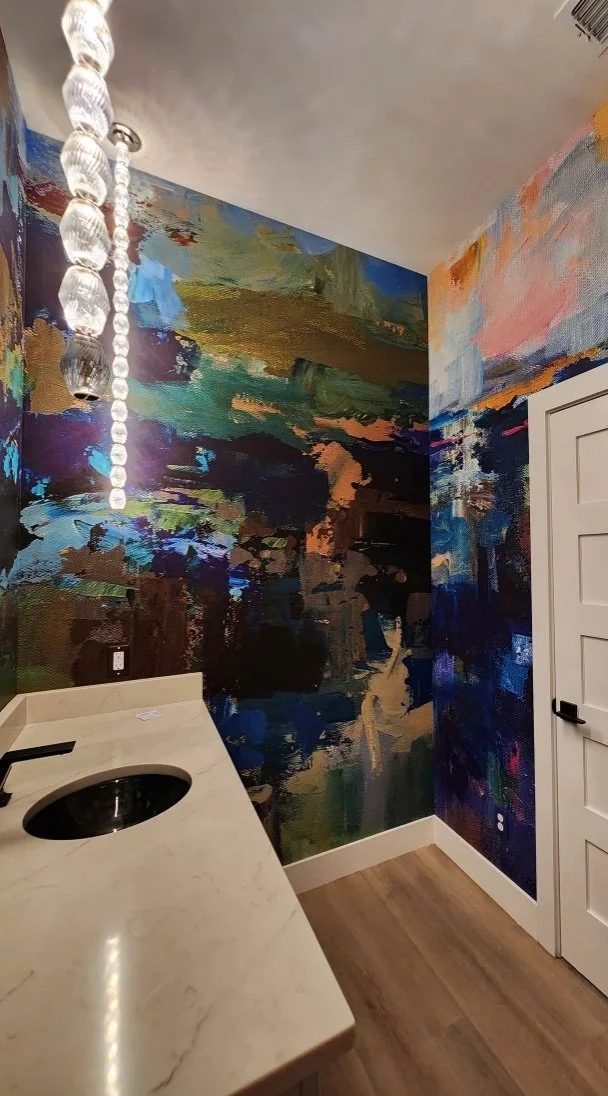 Modern bathroom with abstract colorful painted walls, marble countertop, round sink, hanging glass pendant lights, and wood flooring.