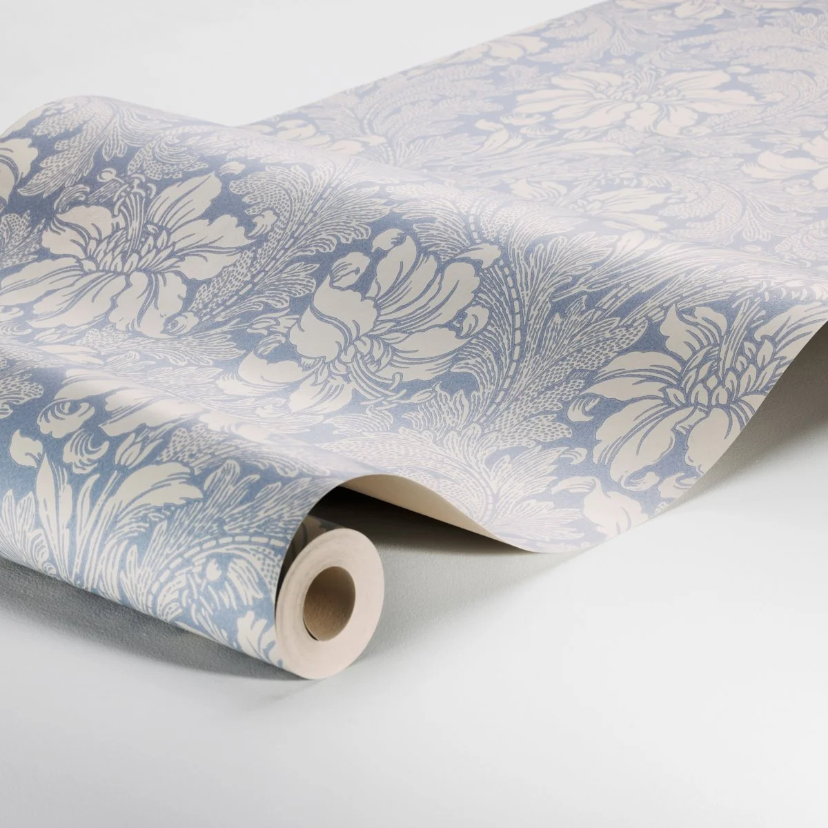 Schumacher Acanthus Garden wallpaper in Blue, unfurled on a roll to show cream blooms, acanthus leaves, and paper texture, SKU 2010