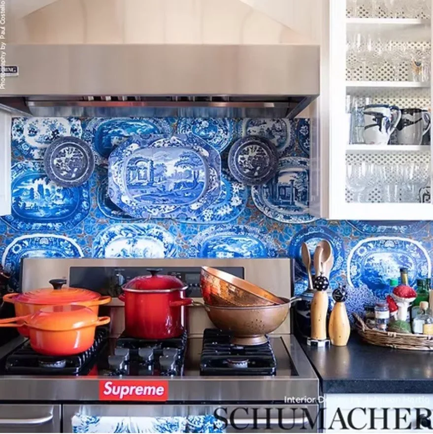 A kitchen stove with red and orange pots, blue-patterned plates on the backsplash, and utensils on the counter.
