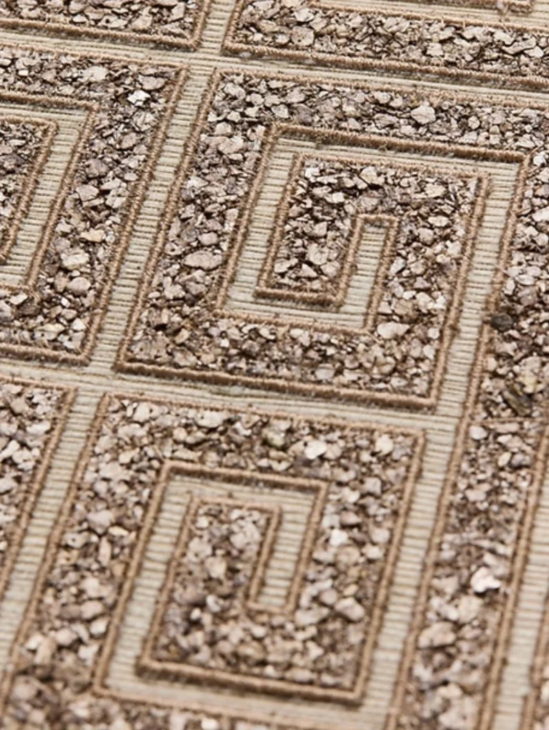 Close-up of a textured beige and brown surface with a repeating geometric Greek key pattern