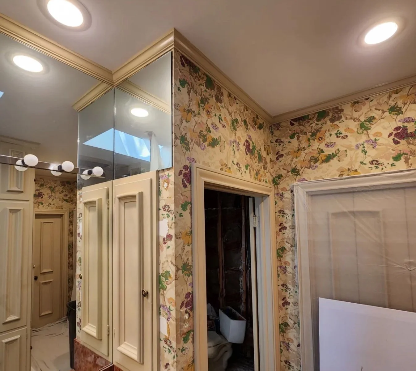 A room under renovation with floral wallpaper, a mirror ceiling, unfinished closet, and construction materials.