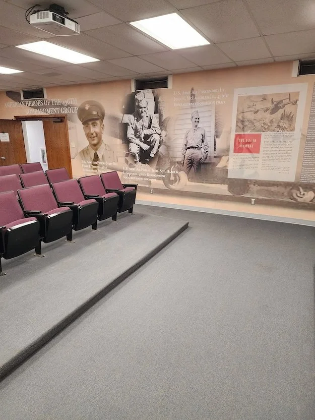 Empty theater room with purple chairs and a large historical mural on the wall featuring black-and-white photos of soldiers and text about American heroes in the Vietnam War.
