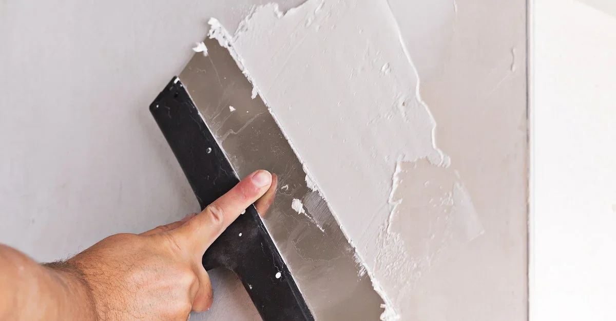 Person applying drywall compound with a putty knife to a wall.