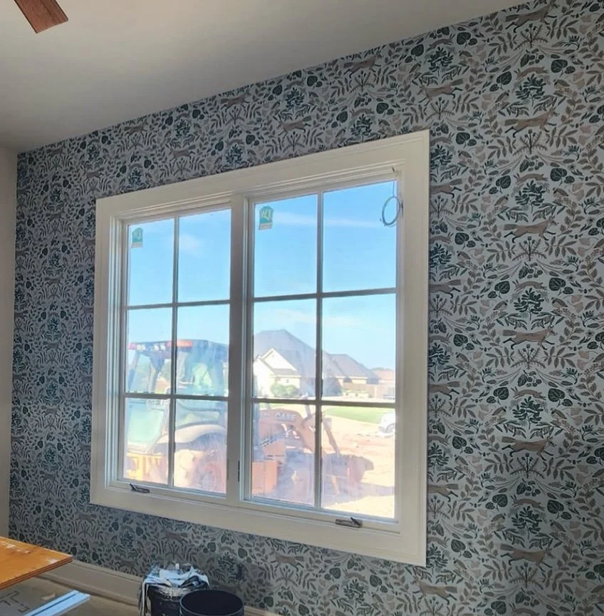 Photo of a window with decorated wallpaper around it, showing a view of a construction site with a vehicle and houses outside.