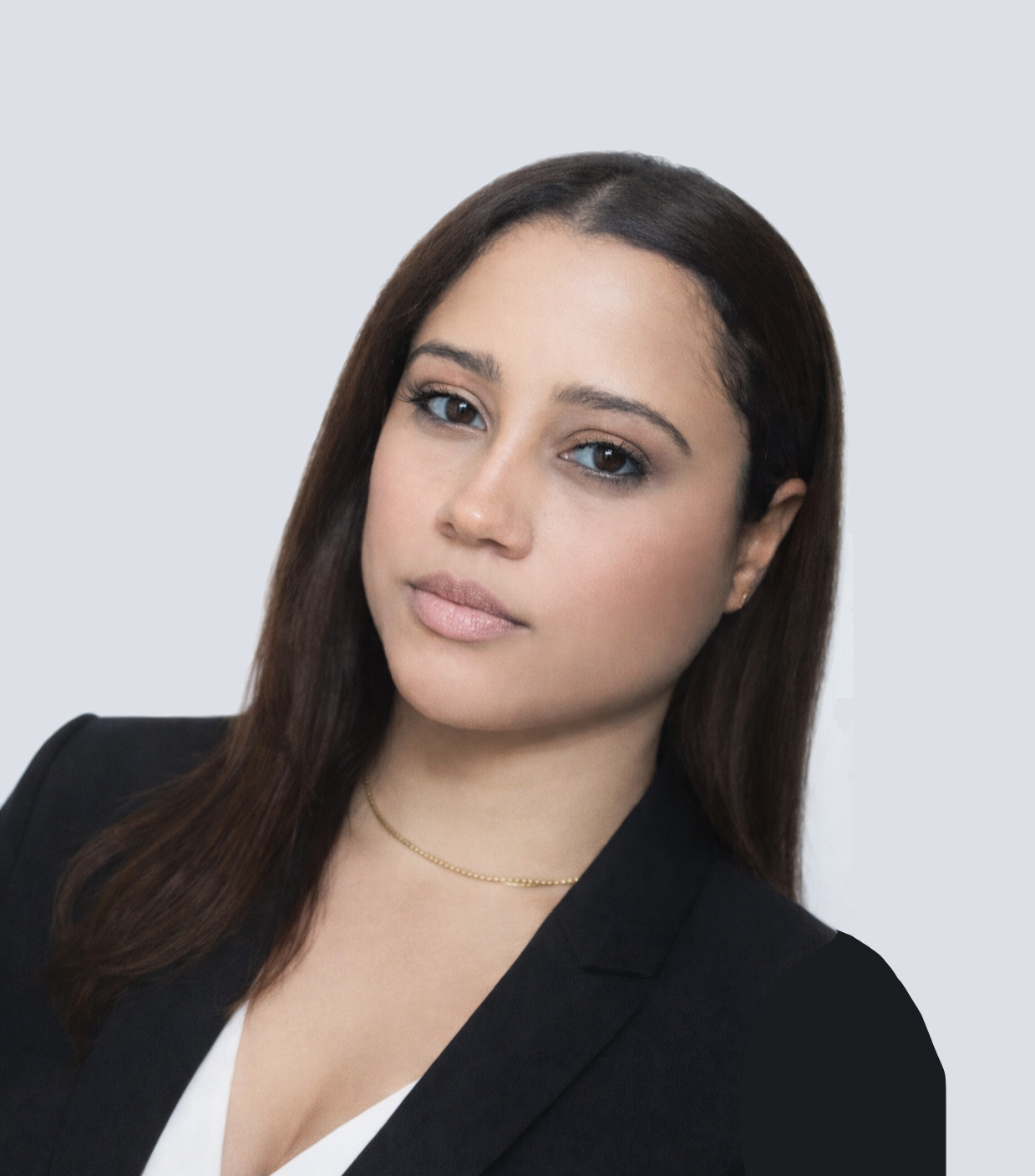 A woman with straight brown hair, wearing a black blazer and a white top, looking at the camera against a plain light gray background.