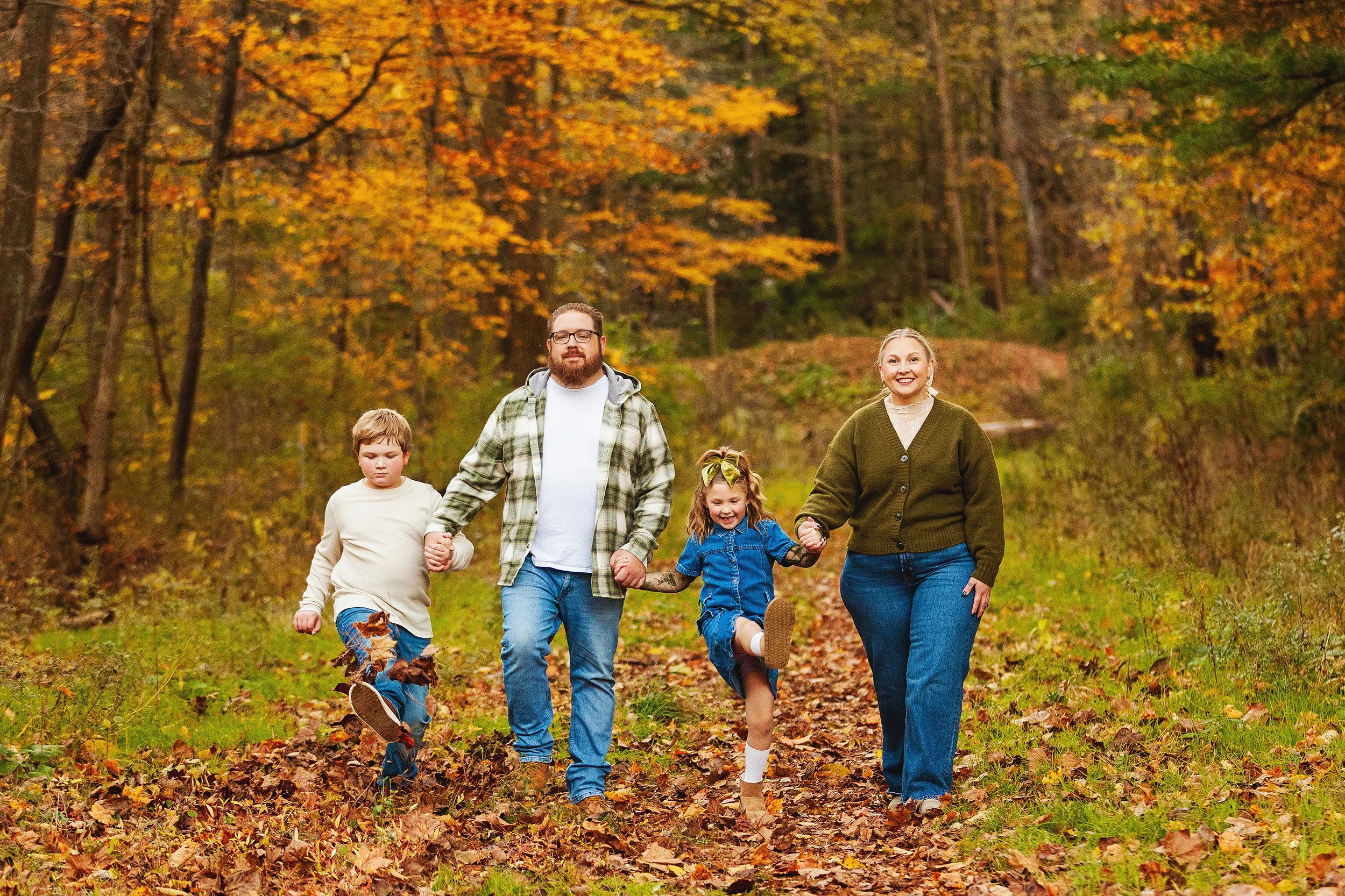 Family walking hand in hand down a leaf covered trail in CVNP during a fall photo session