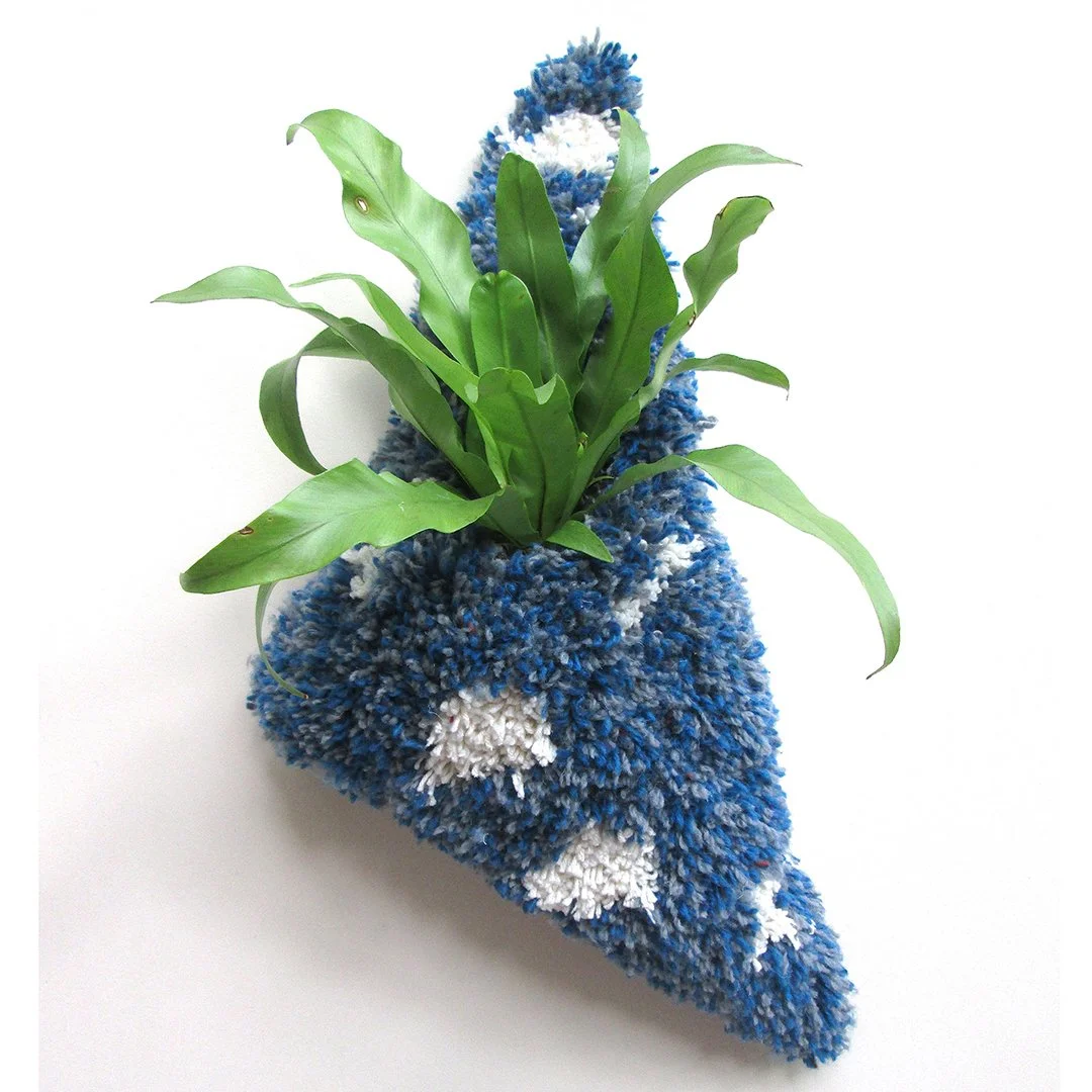 A potted plant with green leaves on a white background, placed on a blue, white, and gray textured cloth.