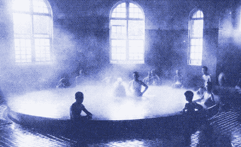 People sitting and standing around an indoor hot spring or pool with steam rising, large arched windows in the background.