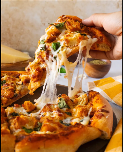 Slice of pizza with melted cheese, chicken, and green herbs being lifted from the pie