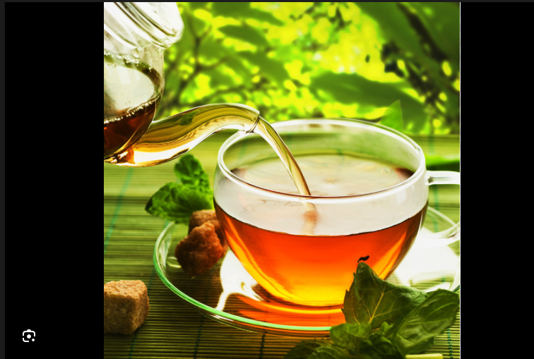 Hot tea being poured into a glass cup, with fresh mint leaves, sugar cubes, and a blurred green outdoor background.