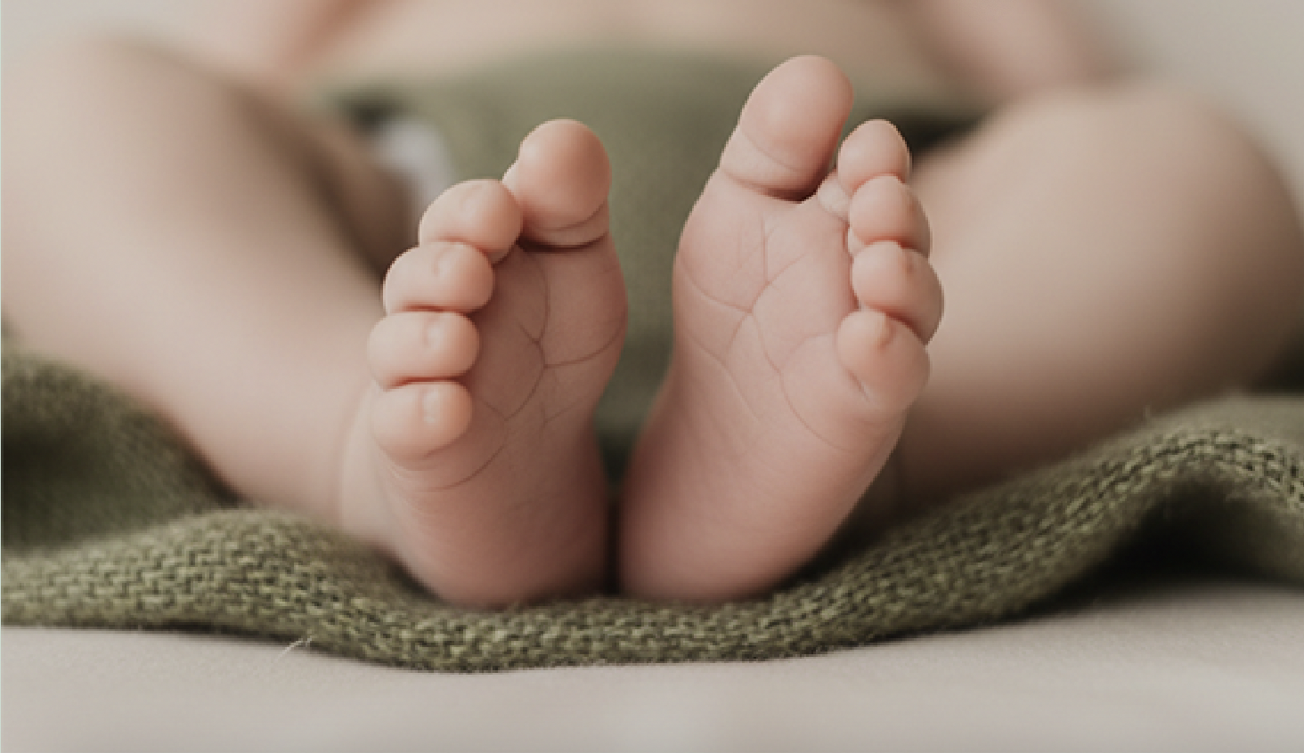 Nahaufnahme von Babyfüßen auf einem Stoffkissen, weiche Haut und kleine Zehen sichtbar.