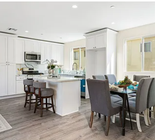 Open-concept kitchen and dining area with white cabinets, island with seating, gray dining chairs, and large windows.