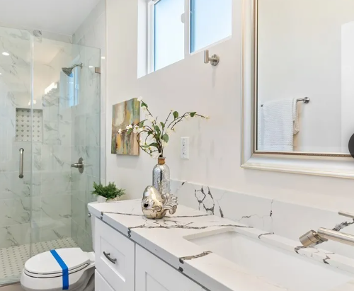 Bathroom with marble countertop, vases, a painting, and a towel rack, with a walk-in shower in the background.