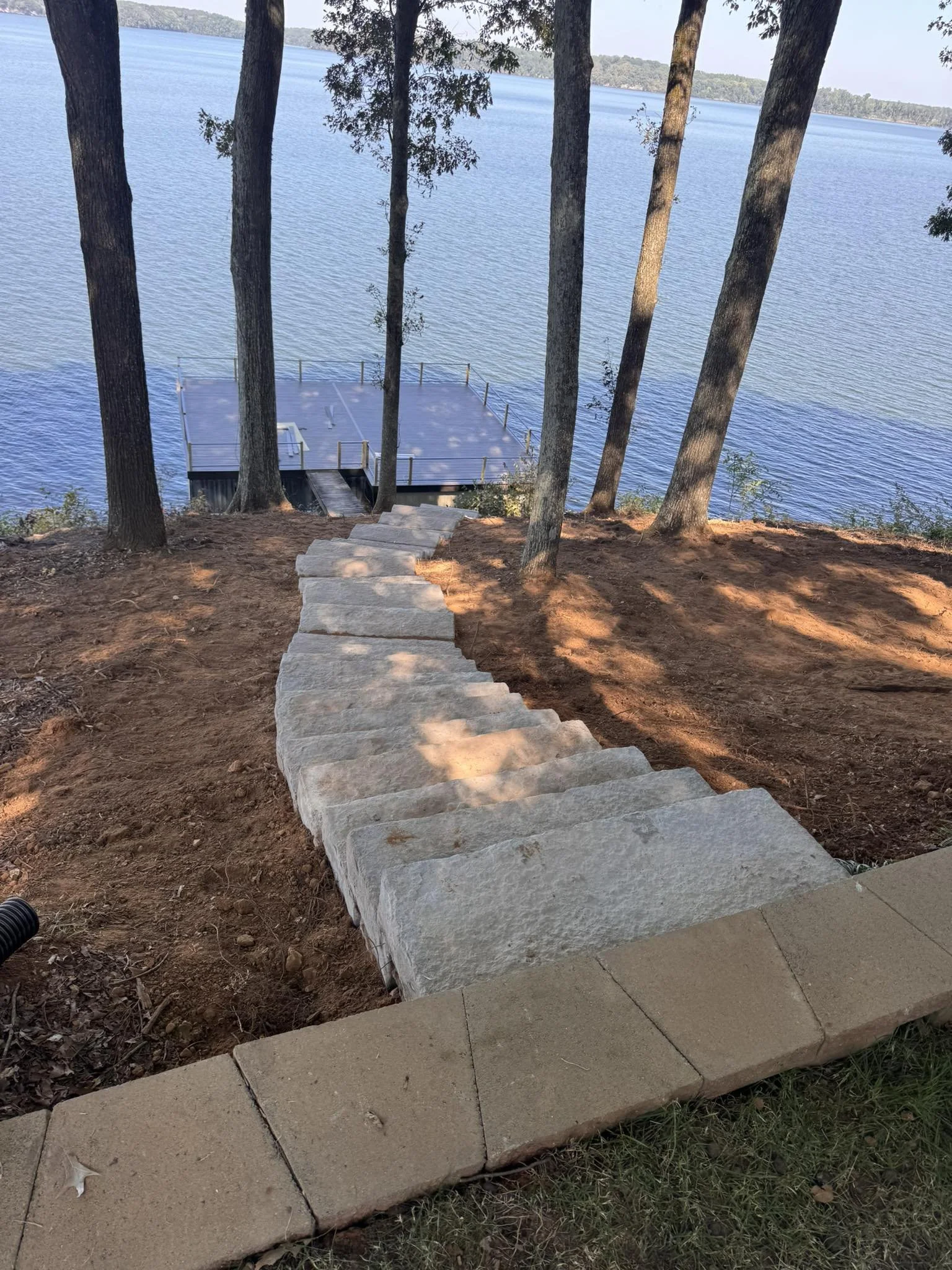 Stone stairs leading down a slope to a dock on a lake, framed by tall trees.