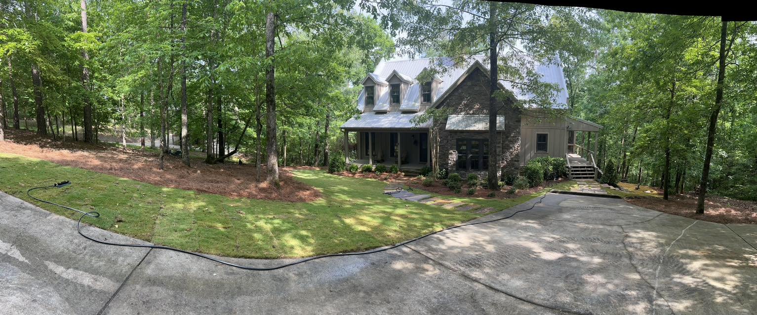 A house in a wooded area with a driveway leading up to it, surrounded by green trees and grass.