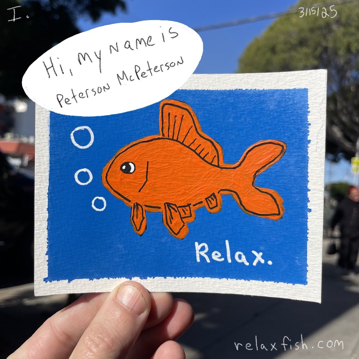 A drawing of an orange fish with bubbles, set against a blue background. Text on the drawing reads 'Relax.' and a speech bubble says 'Hi, my name is Peterson McPetersson.' The illustration appears on a card being held outdoors with trees and people i