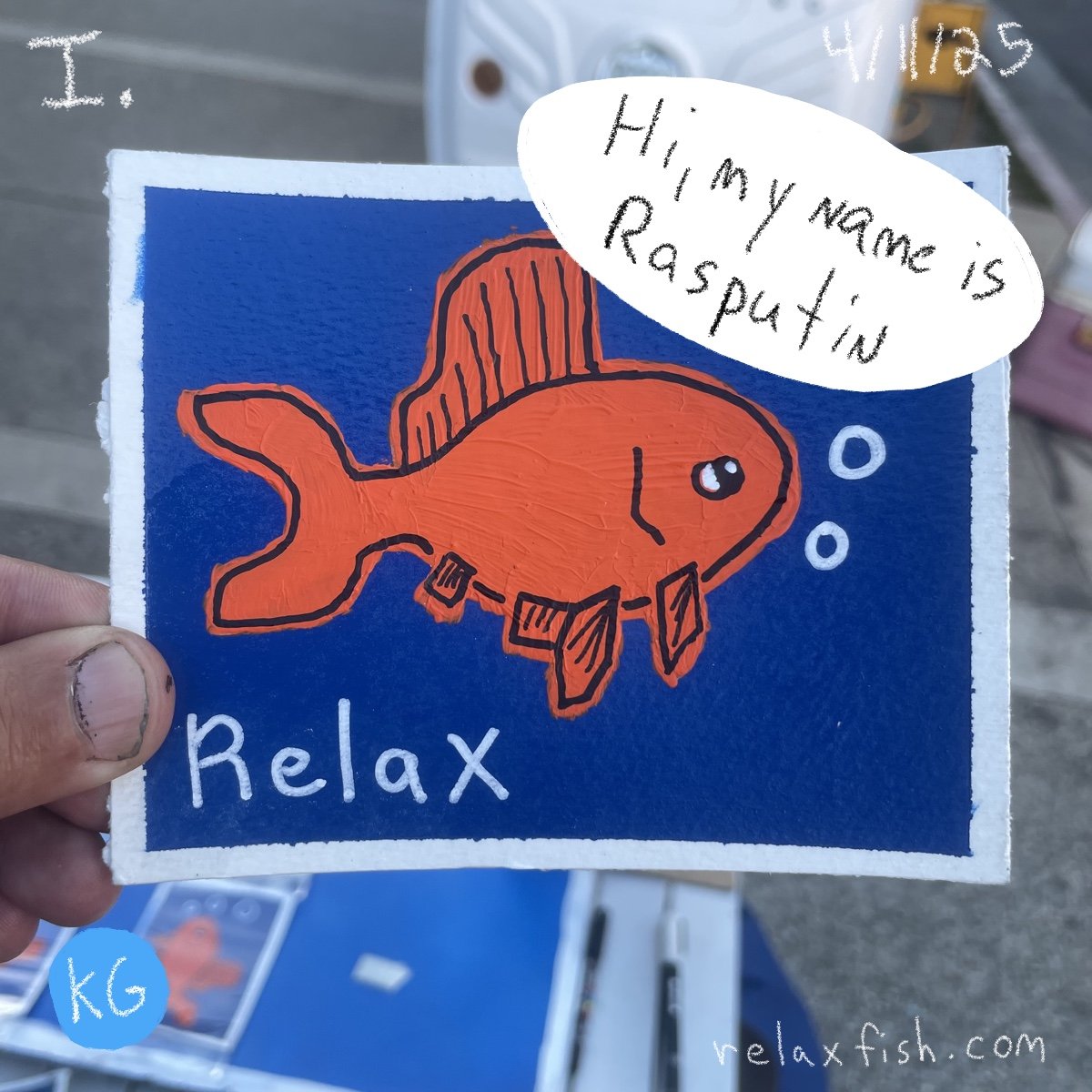 Hand holding a blue card with a drawing of an orange fish wearing a scuba diving mask, with bubbles and the word "Relax" written on it. A speech bubble says, "Hi, my name is Rasputin." The card has a website link "relaxfish.com" and a small blue circ