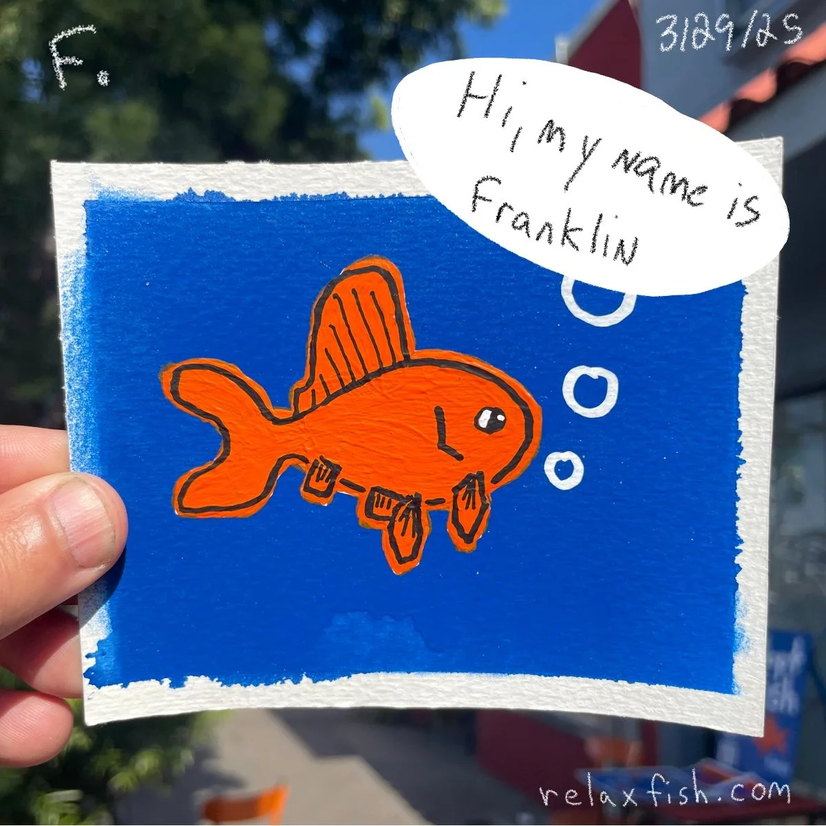 Handwritten sign with an illustration of a cute orange fish with black outlines and white eyes, set against a blue background. The fish is thinking and has a speech bubble that says, 'Hi, my name is Franklin.' There are also some bubbles near the fis