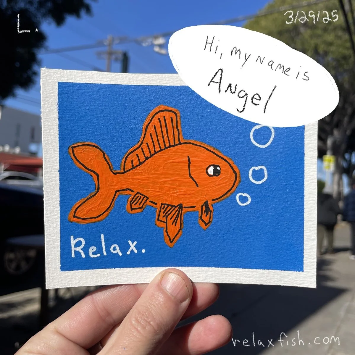 A hand holding a colorful drawing of an orange fish with the word 'Relax' written below it. A speech bubble says, 'Hi, my name is Angel.' The drawing is on textured paper with a blue background, and there is a date in the top right corner. The backgr