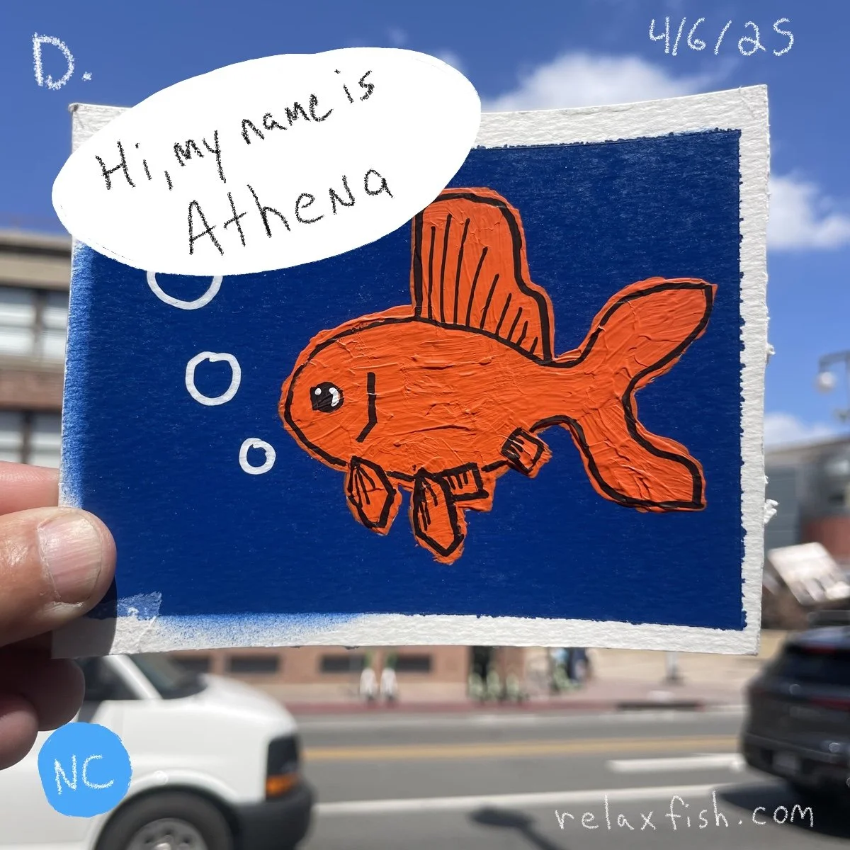 Hand-held painting of an orange fish with black outline on a blue background, with a speech bubble saying 'Hi, my name is Athena,' and the date 4/6/25 in white text at the top right corner.