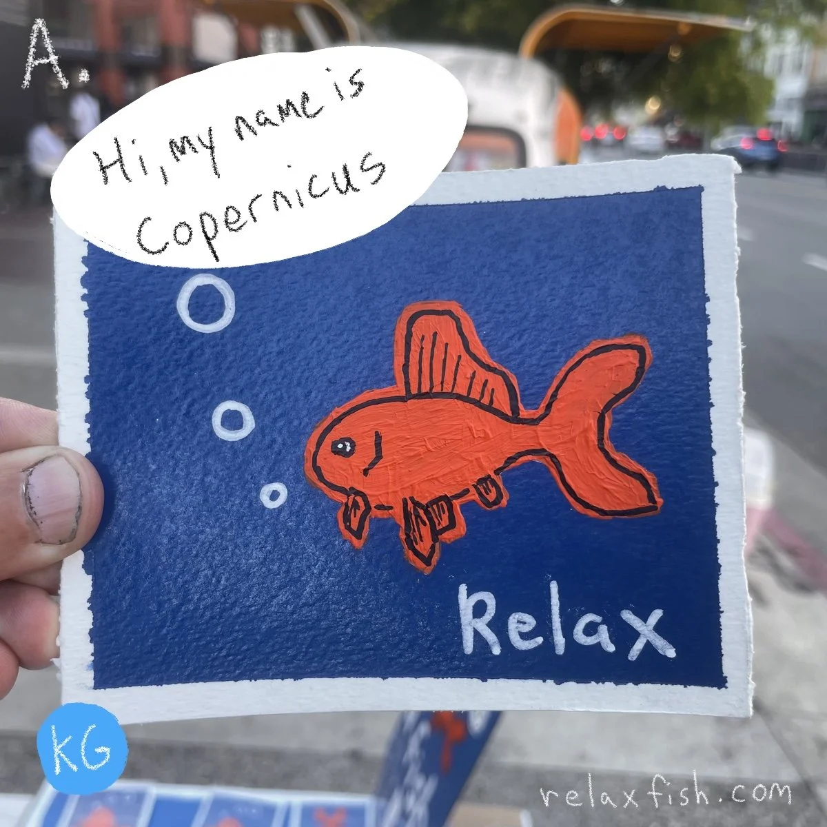 A hand holds a blue card with a drawing of an orange fish and the word "Relax". The fish is blowing bubbles. A speech bubble says, "Hi, my name is Copernicus." The background appears to be a street with cars and trees.
