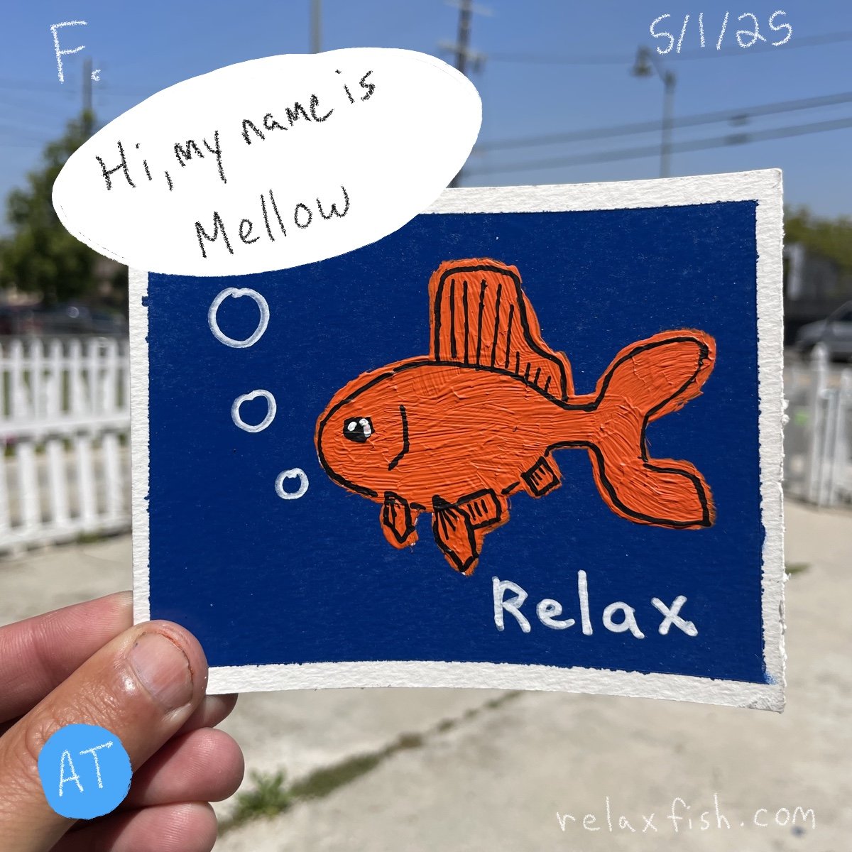 A person holding a blue sign with an orange fish drawing and the words "Relax" and "Hi, my name is Mellow" in a speech bubble. The background features a clear sky, power lines, and a white fence.