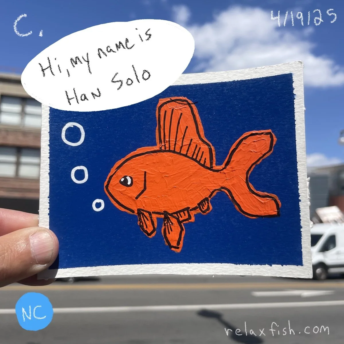 A drawing of an orange fish with a happy expression on a blue background, with a speech bubble saying, "Hi, my name is Han Solo." The drawing appears to be on a piece of paper held up outdoors, with a building, a sidewalk, and a vehicle in the backgr