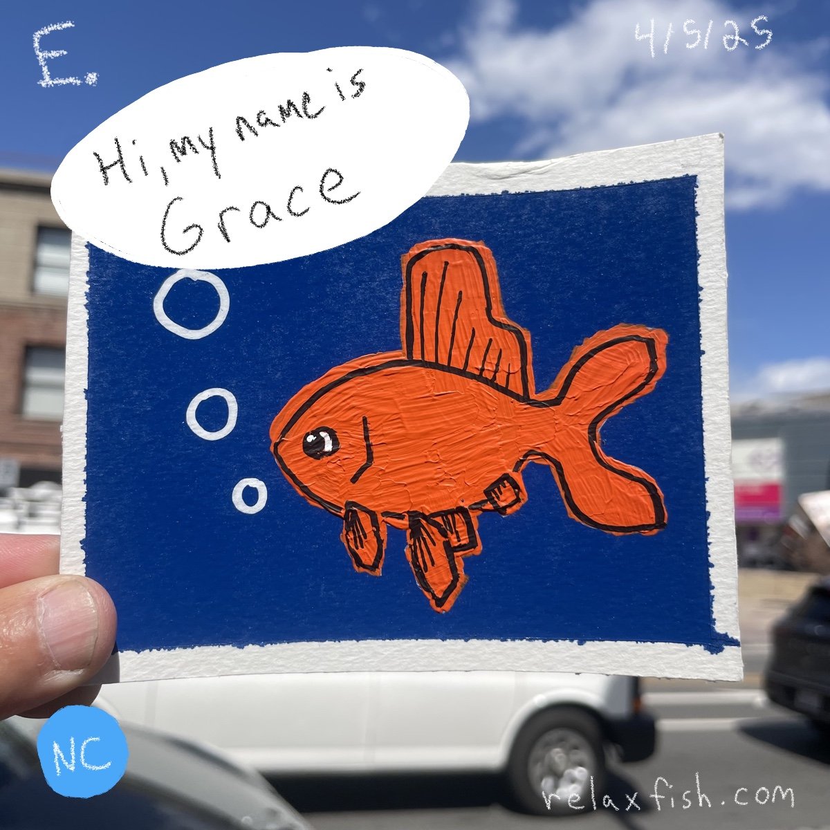 A hand holds up a colorful drawing of an orange fish with fins, set against a blue background. The fish has a smiling face and bubbles coming from its mouth. A speech bubble above says, "Hi, my name is Grace." The drawing appears to be on paper, and 