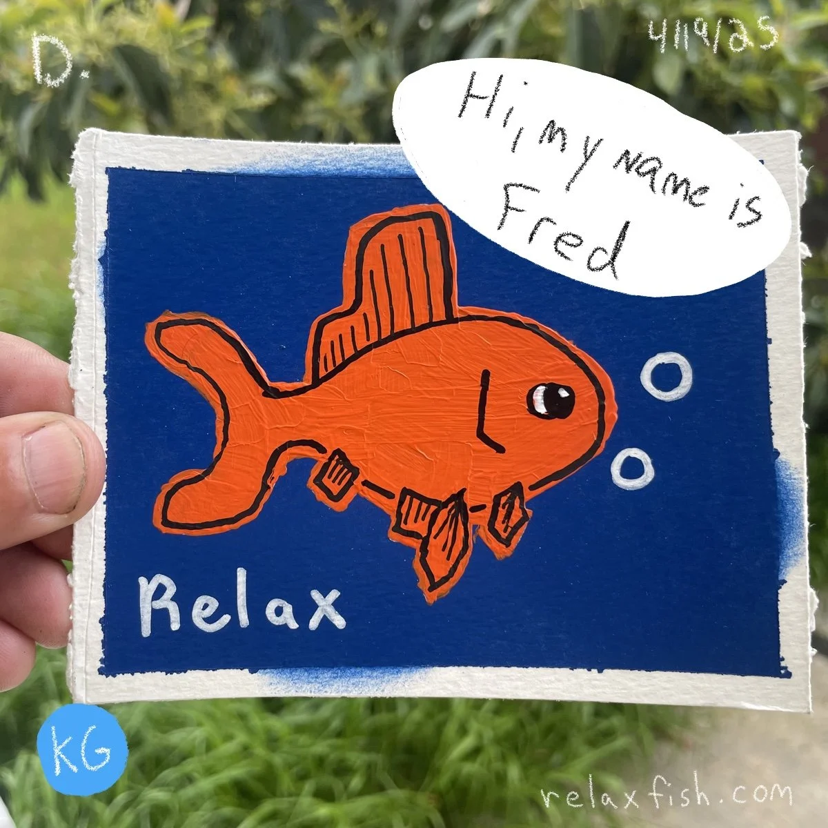 Hand holding a colorful illustration of an orange fish with a hat, bubbles, and a scuba mask, with text "Relax" at the bottom. A speech bubble states "Hi, my name is Fred." The background is dark blue with greenery outside. The image is from a websit