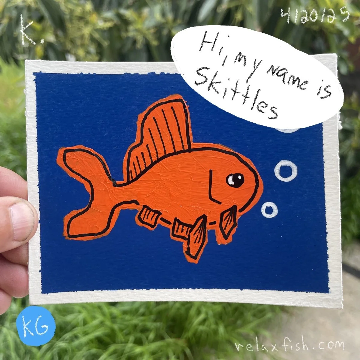 A children's drawing of an orange fish with a scuba diving mask and bubbles on a dark blue background, with a speech bubble saying "Hi, my name is Skitles" and a handwritten note "4/20/23" at the top right corner. The letter "K" is written at the top